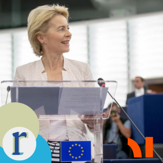 A blonde woman smiling at a lectern bearing the EU flag, inside what looks like the European Parliament chamber — the likeness resembles European Commission President Ursula von der Leyen, though again I'd flag that as my best visual read rather than a confirmed identification.