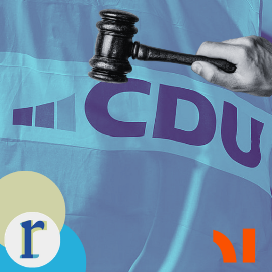 A hand striking a gavel down onto a light-blue flag bearing the logo of the CDU (Christian Democratic Union), a German political party.