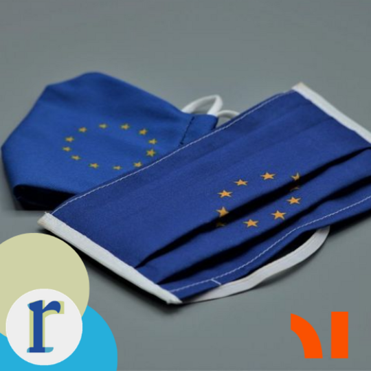 Two folded protective face masks printed with the EU flag's circle of gold stars on a blue background, referencing the COVID-19 pandemic in the EU context.