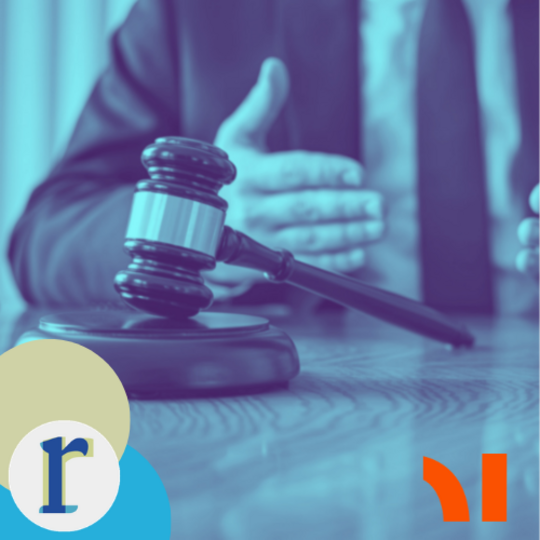A close-up of a judge's hands folded on a desk beside a gavel and sound block, in a blue duotone tint.