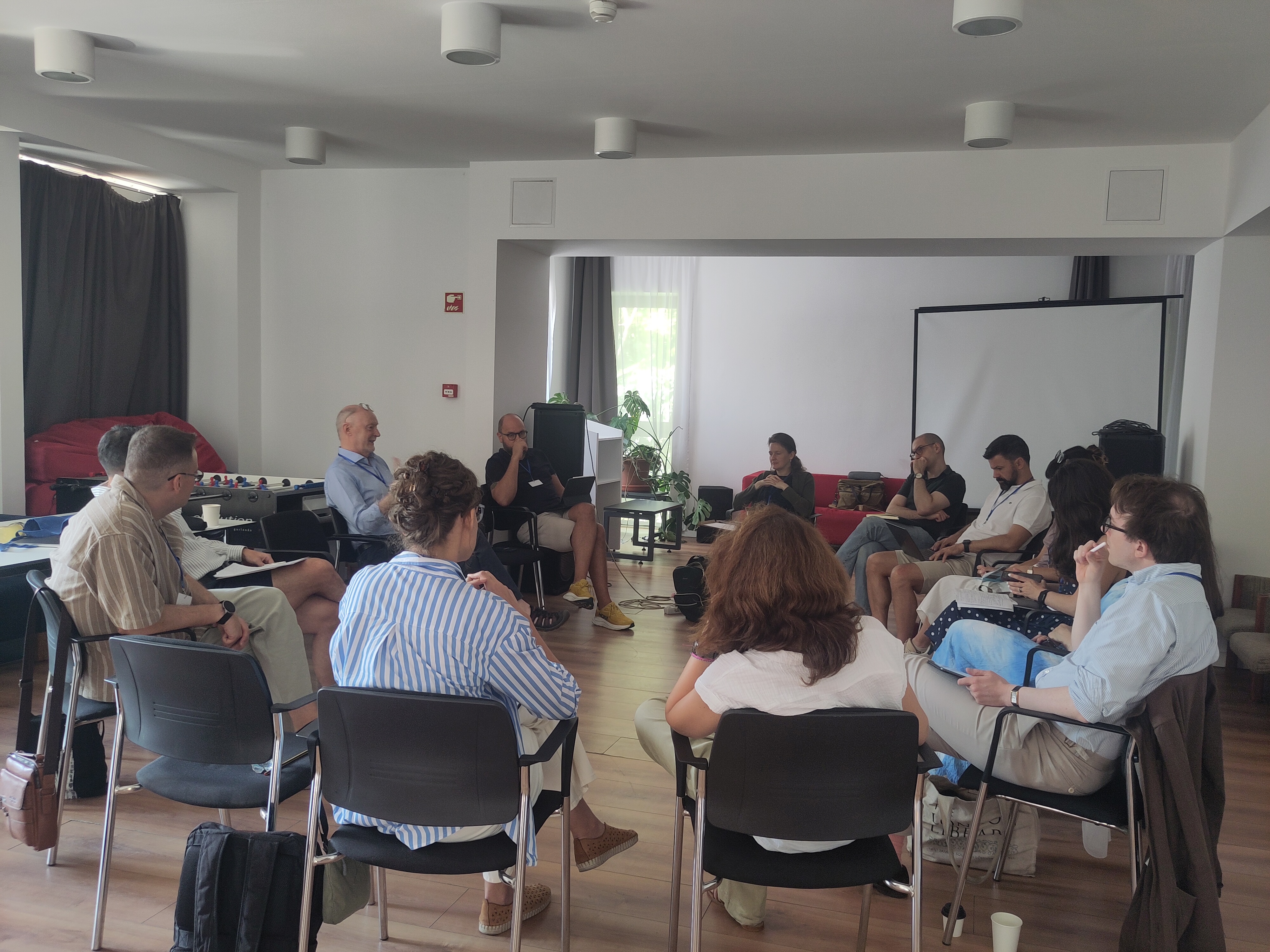 About 12 participants of the summer university are sitting in a circle in a seminar room, engaged in discussion.